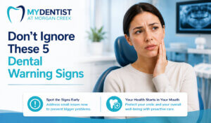 Blog title card for My Dentist at Morgan Creek featuring the headline “Don’t Ignore These 5 Dental Warning Signs” in bold navy and teal text on the left, with the clinic logo above. On the right, a concerned female patient sits in a dental chair holding her jaw, suggesting tooth pain or discomfort, inside a modern dental clinic setting. Along the bottom are two icons with short messages encouraging early detection and proactive dental care. The design uses the clinic’s blue and teal brand colours in a clean, professional layout.