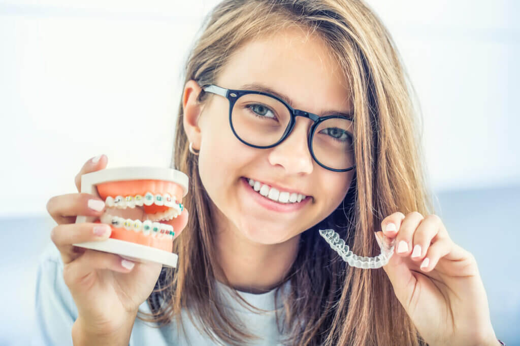 A girl holding a jaw with metal braces and an Invisalign aligner tray