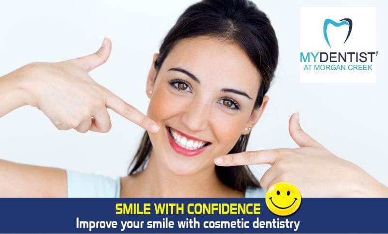Cosmetic Dentistry in South Surrey at My Dentist at Morgan Creek. A young woman smiling and pointing to her beautiful white teeth