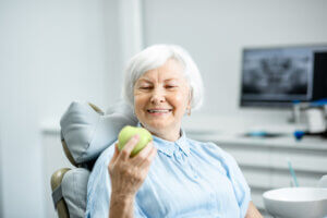 Happy female senior citizen holding an apple after getting her dental implants