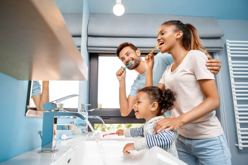 a young family (husband, wife and daughter) brushing their teeth together and having fun as instructed by their Surrey Family dentist