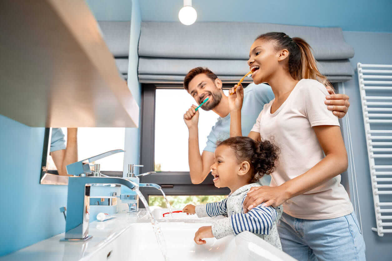 a young family (husband, wife and daughter) brushing their teeth together and having fun as instructed by their Surrey Family dentist
