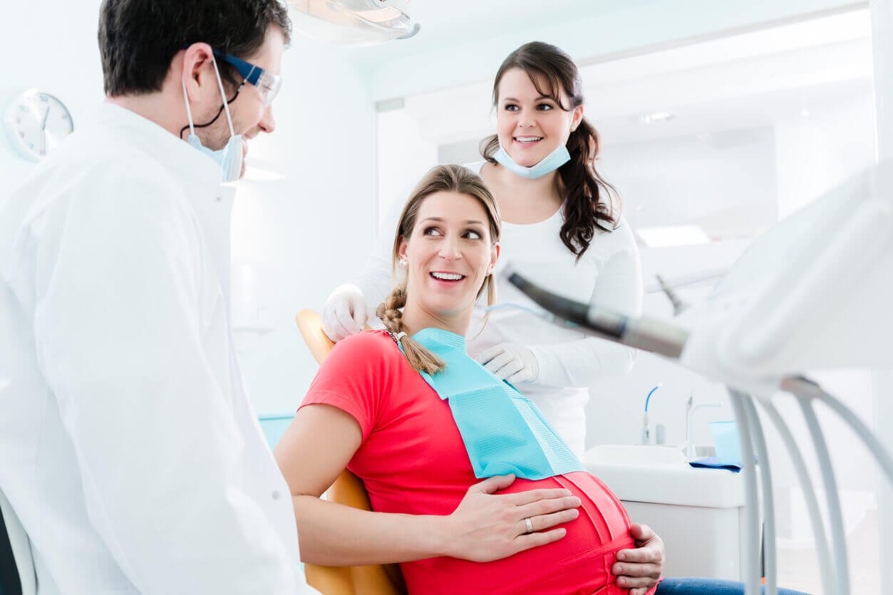 A pregnant woman at a dental office discussing oral health and pregnancy with two dental health professionals