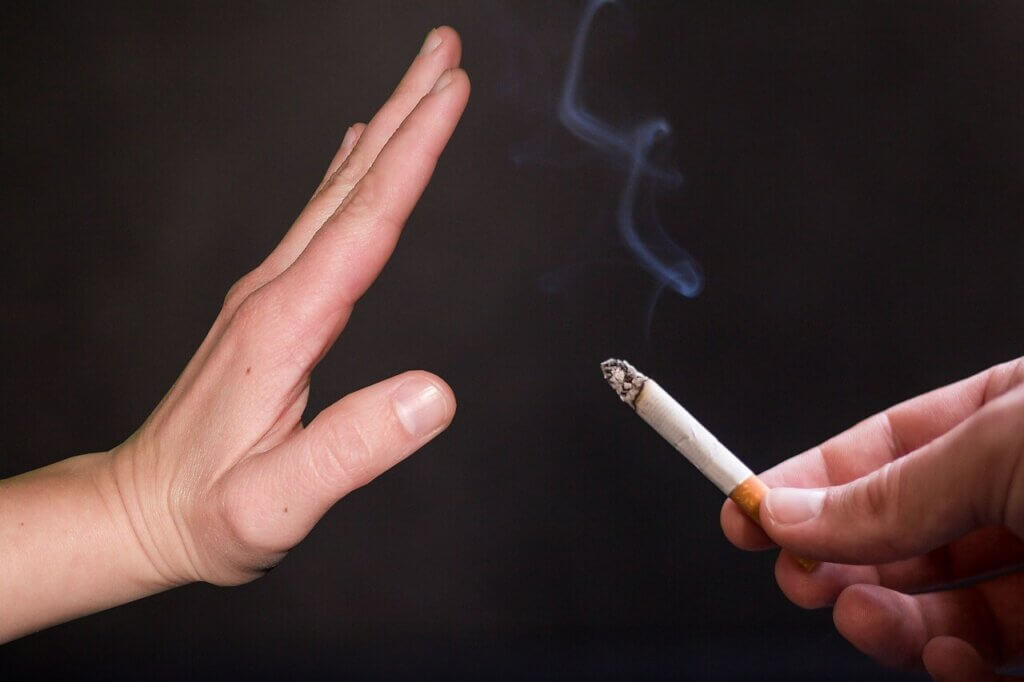 two hands - one holding a cigarette while the other indicating stop smoking