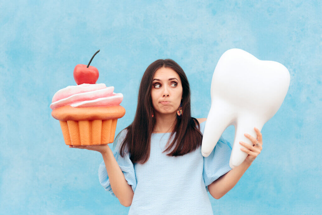 a young woman holding a cupcake on one hand a a giant tooth on the other