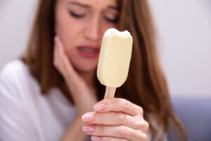 A woman holding an ice cream and experiencing tooth pain due to tooth sensitivity to cold