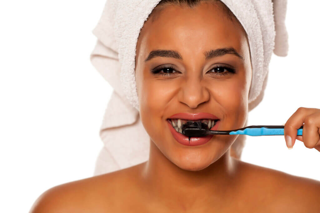 portrait of a happy young dark-skinned woman brushing her teeth with black charcoal toothpaste on a white background